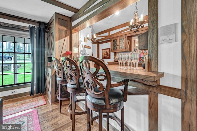 bar with light hardwood / wood-style flooring, an inviting chandelier, beam ceiling, and pendant lighting