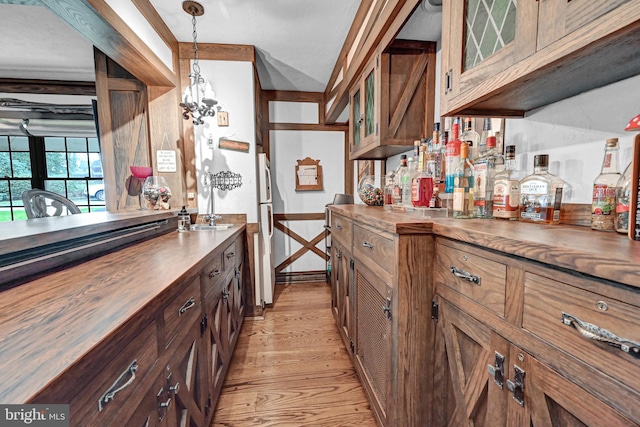 bar with butcher block countertops, a notable chandelier, light wood-type flooring, and hanging light fixtures