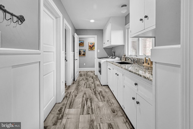 kitchen featuring sink, white cabinetry, light stone counters, and washer and clothes dryer