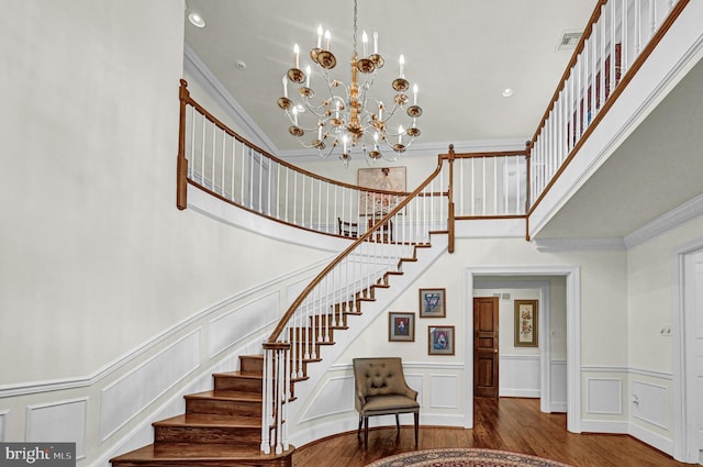 stairway with ornamental molding, a notable chandelier, wood-type flooring, and a towering ceiling