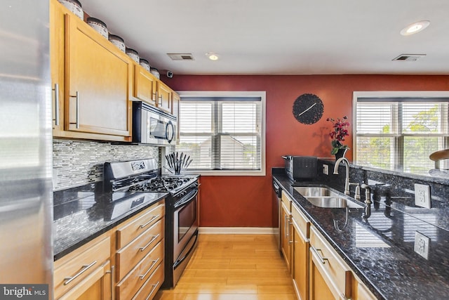 kitchen featuring backsplash, stainless steel appliances, light hardwood / wood-style floors, dark stone countertops, and sink