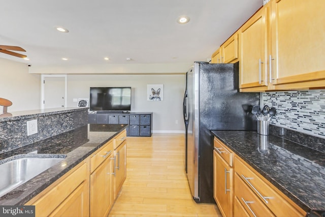 kitchen featuring black fridge, tasteful backsplash, dark stone countertops, light hardwood / wood-style floors, and ceiling fan