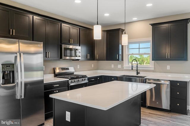 kitchen featuring a kitchen island, a sink, appliances with stainless steel finishes, light wood finished floors, and decorative light fixtures