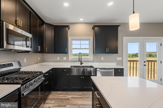 kitchen with recessed lighting, a sink, appliances with stainless steel finishes, light stone countertops, and decorative light fixtures