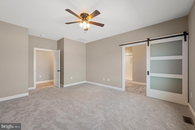 unfurnished bedroom with visible vents, a barn door, a ceiling fan, light carpet, and baseboards