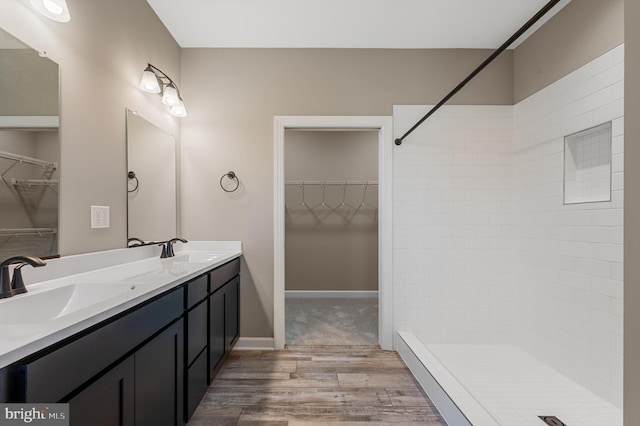 bathroom with a walk in closet, double vanity, a sink, and wood finished floors