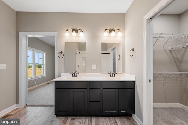 full bathroom with double vanity, baseboards, a sink, and wood finished floors