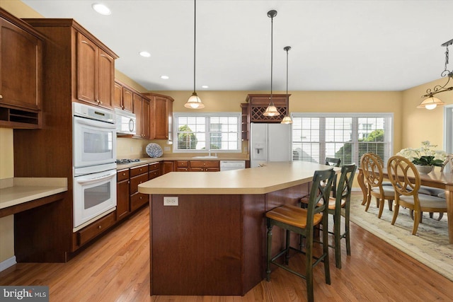 kitchen featuring decorative light fixtures, white appliances, sink, a breakfast bar area, and light hardwood / wood-style floors