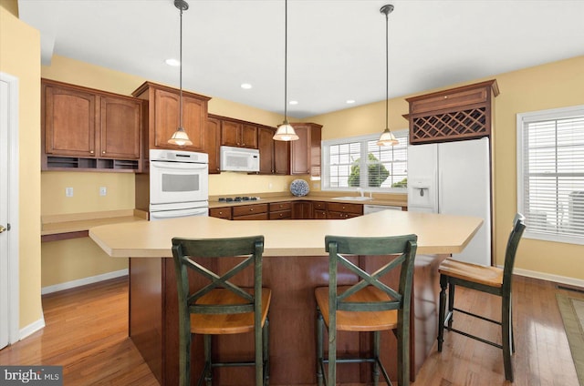 kitchen featuring a kitchen breakfast bar, white appliances, light wood-type flooring, and decorative light fixtures