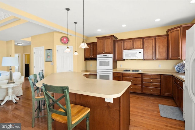 kitchen with wood-type flooring, white appliances, pendant lighting, and a kitchen breakfast bar