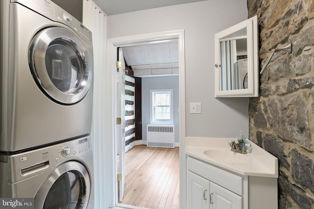 washroom with stacked washer / dryer, sink, radiator, and light wood-type flooring