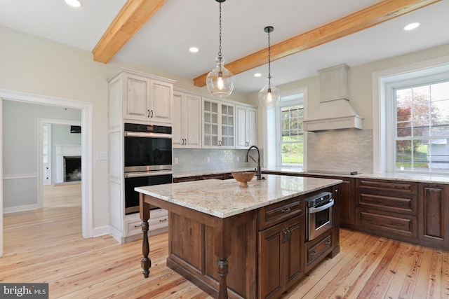 kitchen with dark brown cabinetry, custom exhaust hood, tasteful backsplash, light wood-type flooring, and stainless steel double oven