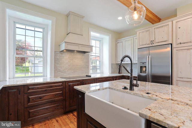 kitchen featuring stainless steel fridge with ice dispenser, hanging light fixtures, backsplash, light hardwood / wood-style floors, and custom exhaust hood