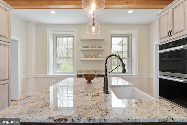 kitchen with a kitchen island, hanging light fixtures, double oven, light stone counters, and sink