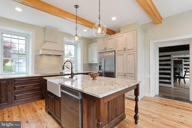 kitchen featuring a kitchen island with sink, stainless steel appliances, light stone counters, tasteful backsplash, and light hardwood / wood-style floors