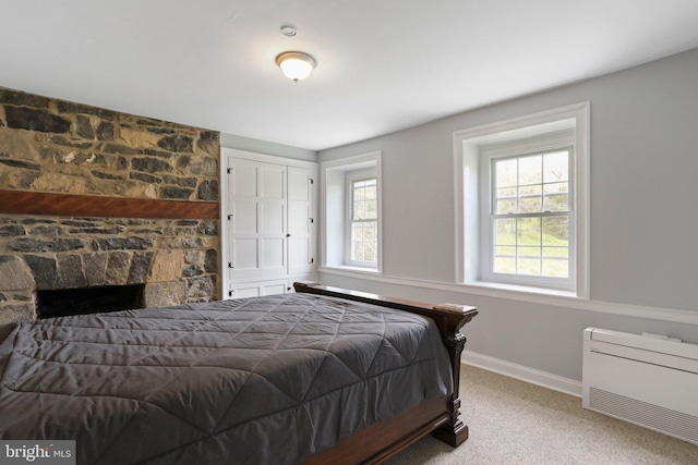 bedroom featuring light colored carpet and a stone fireplace