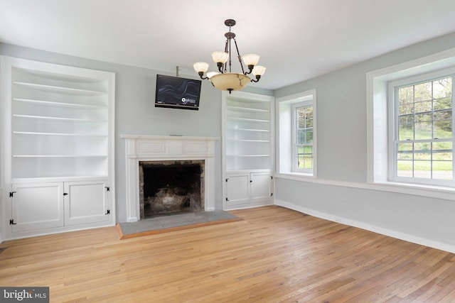 unfurnished living room featuring a wealth of natural light, a notable chandelier, light wood-type flooring, and built in features