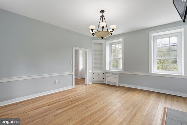 empty room with a wealth of natural light, a notable chandelier, light wood-type flooring, and radiator heating unit