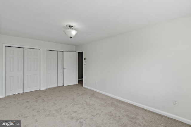 unfurnished bedroom featuring light colored carpet and multiple closets