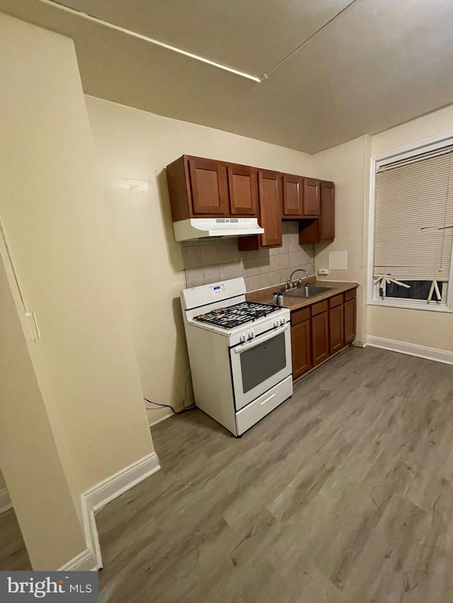 kitchen with sink, light wood-type flooring, tasteful backsplash, and white gas range