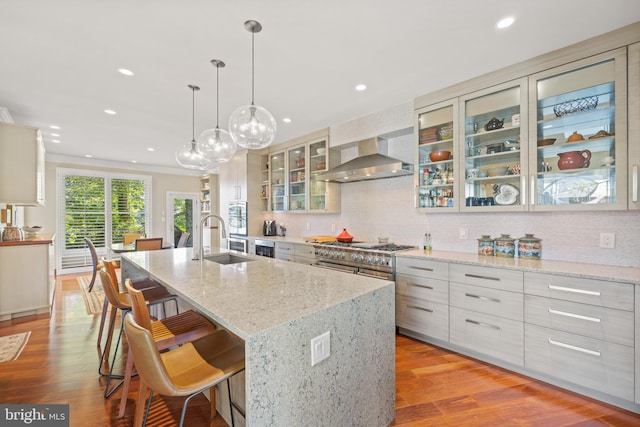 kitchen featuring a spacious island, wall chimney range hood, sink, light wood-type flooring, and decorative light fixtures