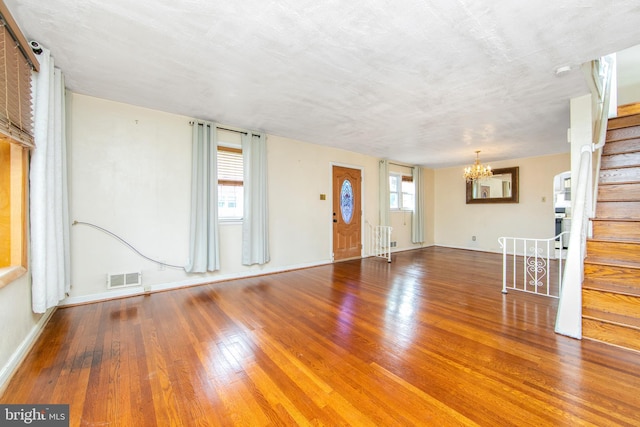 unfurnished living room with a chandelier, a textured ceiling, hardwood / wood-style flooring, and a wealth of natural light