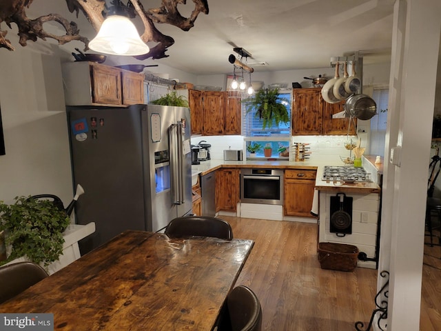 kitchen featuring decorative light fixtures, light hardwood / wood-style floors, tasteful backsplash, and stainless steel appliances