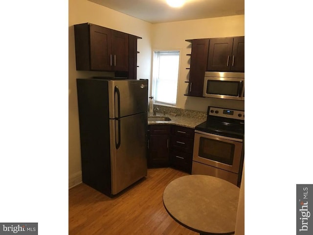 kitchen with stainless steel appliances, dark brown cabinets, light wood-type flooring, and sink