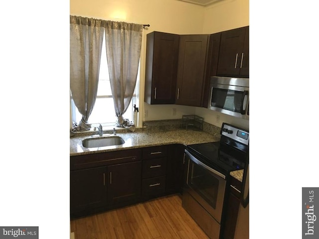 kitchen with light hardwood / wood-style floors, stone countertops, range with electric stovetop, dark brown cabinets, and sink