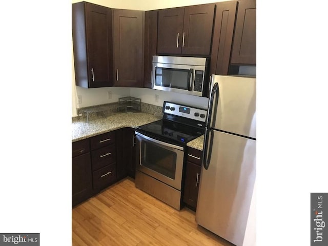 kitchen with light stone countertops, light hardwood / wood-style floors, dark brown cabinets, and appliances with stainless steel finishes