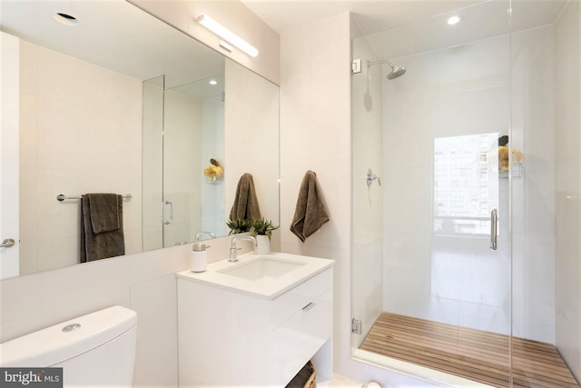 bathroom with toilet, vanity, a shower with door, and tile walls