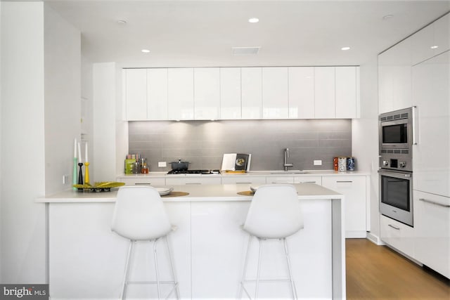 kitchen with white cabinets, light hardwood / wood-style flooring, tasteful backsplash, and stainless steel appliances