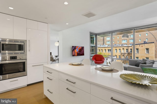 kitchen with appliances with stainless steel finishes, a wall of windows, light hardwood / wood-style flooring, and white cabinets