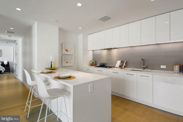 kitchen with white cabinets, sink, a breakfast bar area, light hardwood / wood-style floors, and tasteful backsplash