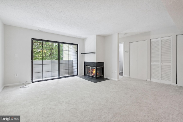 unfurnished living room with dark colored carpet, a multi sided fireplace, and a textured ceiling