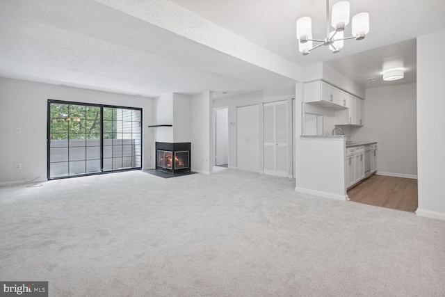 unfurnished living room with sink, an inviting chandelier, a multi sided fireplace, a textured ceiling, and light carpet