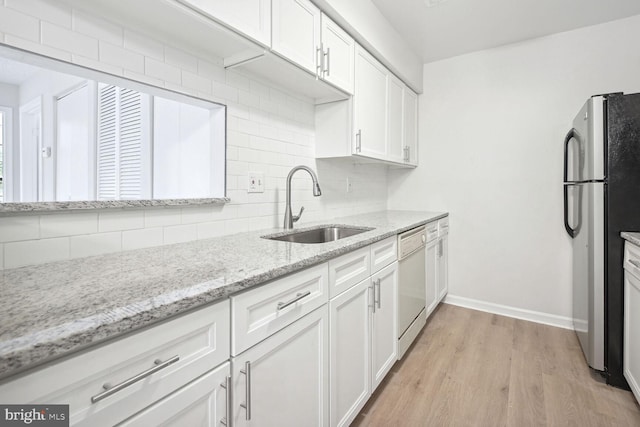 kitchen with dishwasher, sink, white cabinets, stainless steel fridge, and light stone countertops