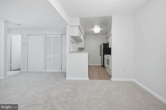 kitchen with white cabinetry, a textured ceiling, light carpet, electric range, and stainless steel fridge