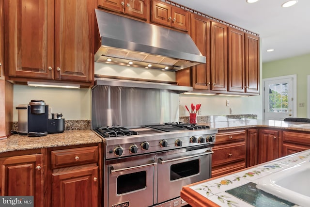 kitchen featuring exhaust hood, light stone counters, and range with two ovens