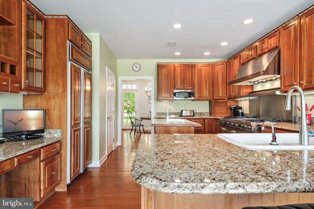 kitchen with exhaust hood, light stone countertops, dark hardwood / wood-style floors, and a kitchen island