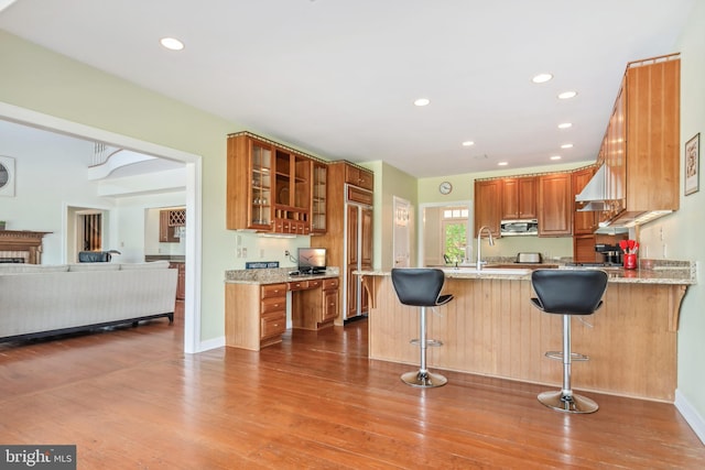 kitchen with paneled fridge, kitchen peninsula, hardwood / wood-style floors, a breakfast bar, and light stone counters