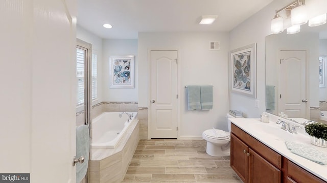 bathroom with vanity, toilet, and tiled bath