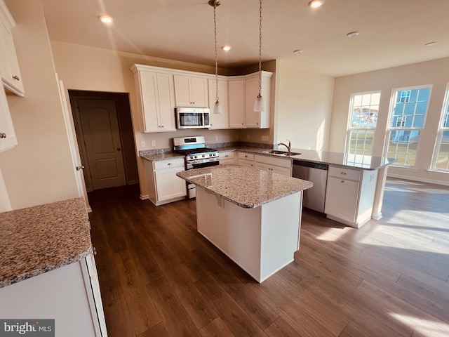 kitchen with kitchen peninsula, white cabinetry, stainless steel appliances, light stone counters, and dark hardwood / wood-style flooring