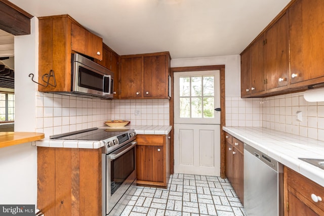 kitchen featuring tile countertops, backsplash, stainless steel appliances, and a healthy amount of sunlight