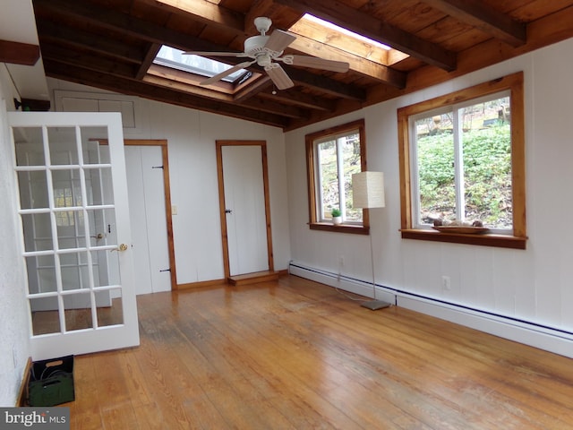 empty room with vaulted ceiling with skylight, ceiling fan, light wood-type flooring, a baseboard radiator, and wood ceiling