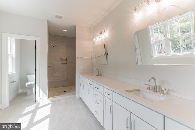 bathroom with tiled shower, toilet, tile floors, and dual vanity