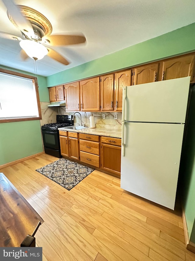 kitchen featuring sink, ceiling fan, black range with gas stovetop, white fridge, and light hardwood / wood-style floors