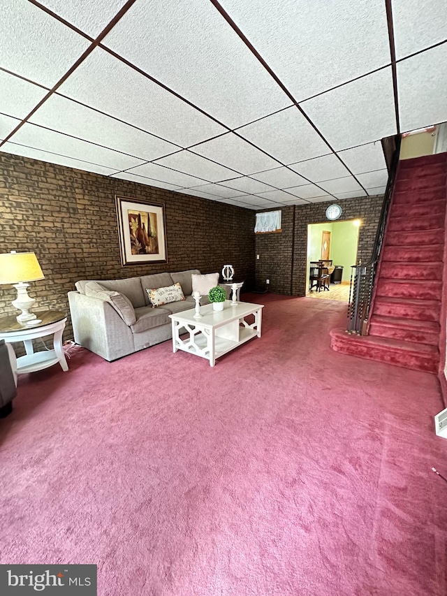 unfurnished living room with brick wall, carpet, and a paneled ceiling