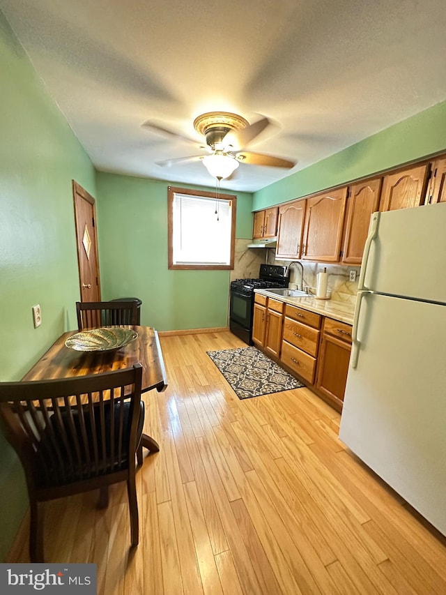 kitchen featuring light wood-type flooring, white fridge, ceiling fan, sink, and black gas range