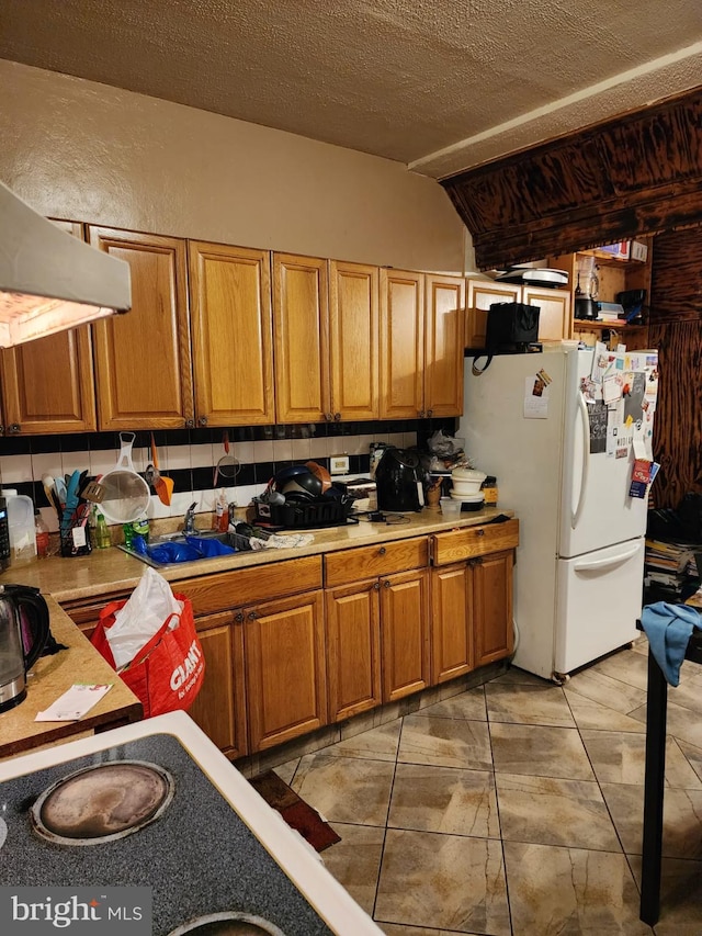 kitchen with white refrigerator, light tile floors, sink, fume extractor, and lofted ceiling